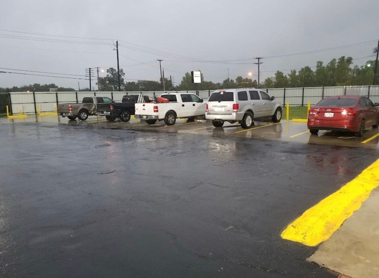 Un estacionamiento con varios vehículos, incluyendo camionetas y un coche rojo, y una línea amarilla que marca el borde.