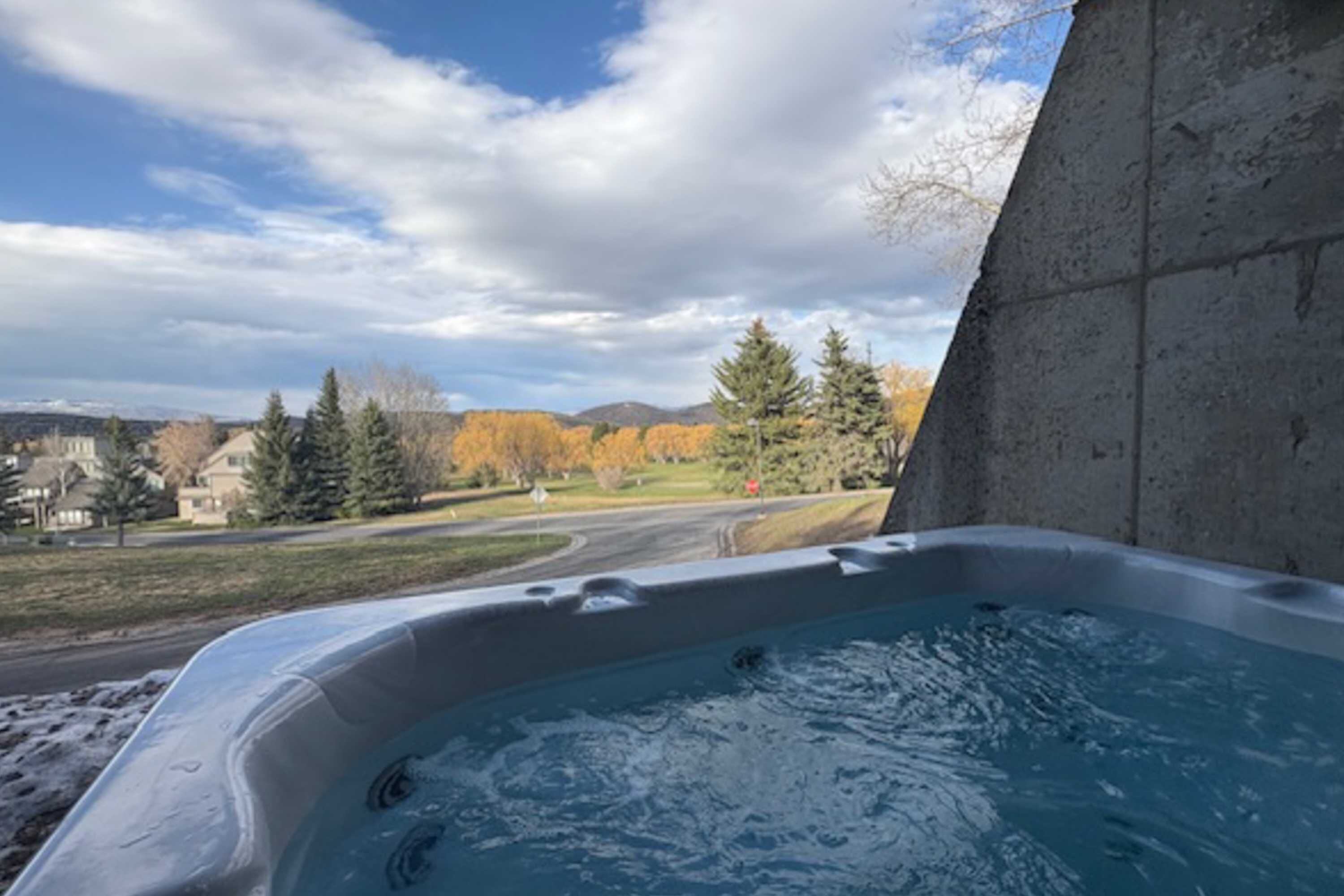 Un jacuzzi con vista a una carretera, árboles y montañas lejanas.