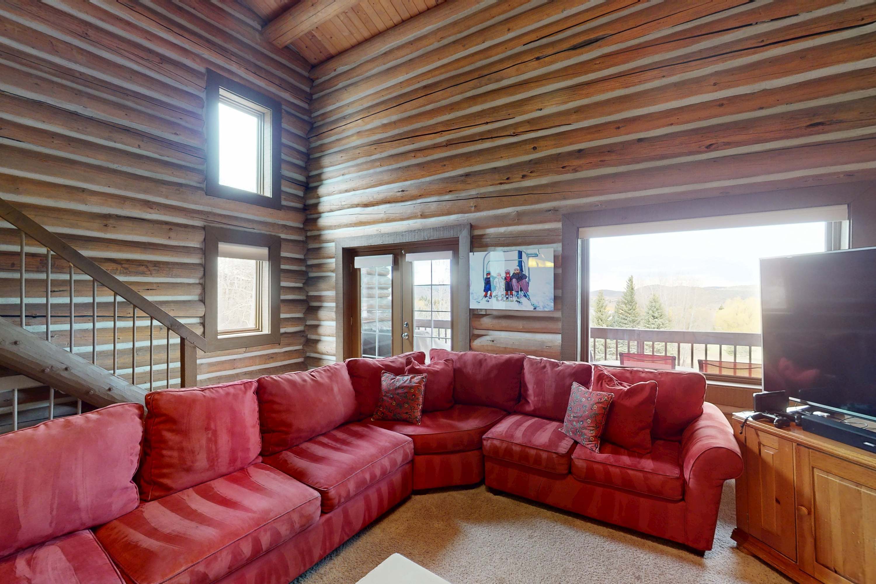 A log cabin interior with a red sectional sofa, a television, and a staircase.
