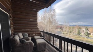 Eine Holzterrasse mit Korbmöbeln, einem schwarzen Geländer und Blick auf eine Wohngegend.