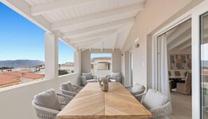 Ein Balkon mit Holztisch und Korbstühlen, Blick auf die Stadtlandschaft und einen klaren Himmel.