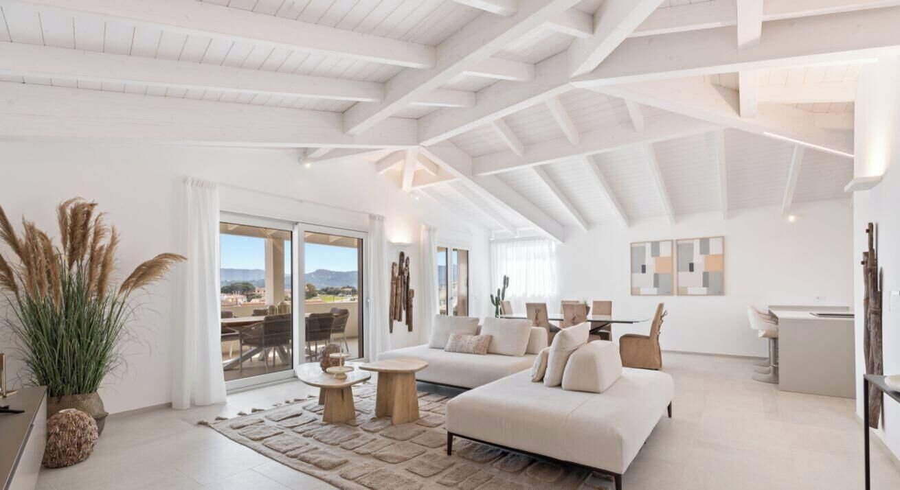 A spacious living room with a high ceiling, a large sofa, a dining area, and a view of the outdoors.