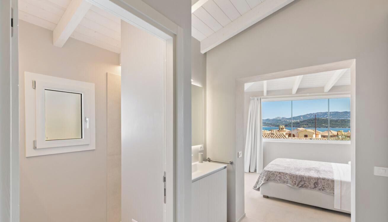 A bedroom with a bed, a window with a view, a door, and a mirror.