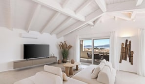 A modern living room with a flat-screen TV, a sofa, a coffee table, and a view of the outdoors through large sliding doors. - Appartamento Ginevra 6 (Arzachena)