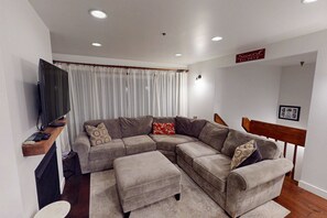 Een woonkamer met een modulaire bank, een flatscreen televisie, een houten plank en een trap.