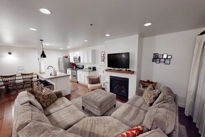 A living room with a sofa, a television, a fireplace, and a kitchen area in the background. - Dog-friendly Old Town Empire Condo near resort with  ski storage (Park City)