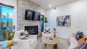Una sala moderna con chimenea de piedra, un televisor de pantalla plana y un cuadro abstracto grande.