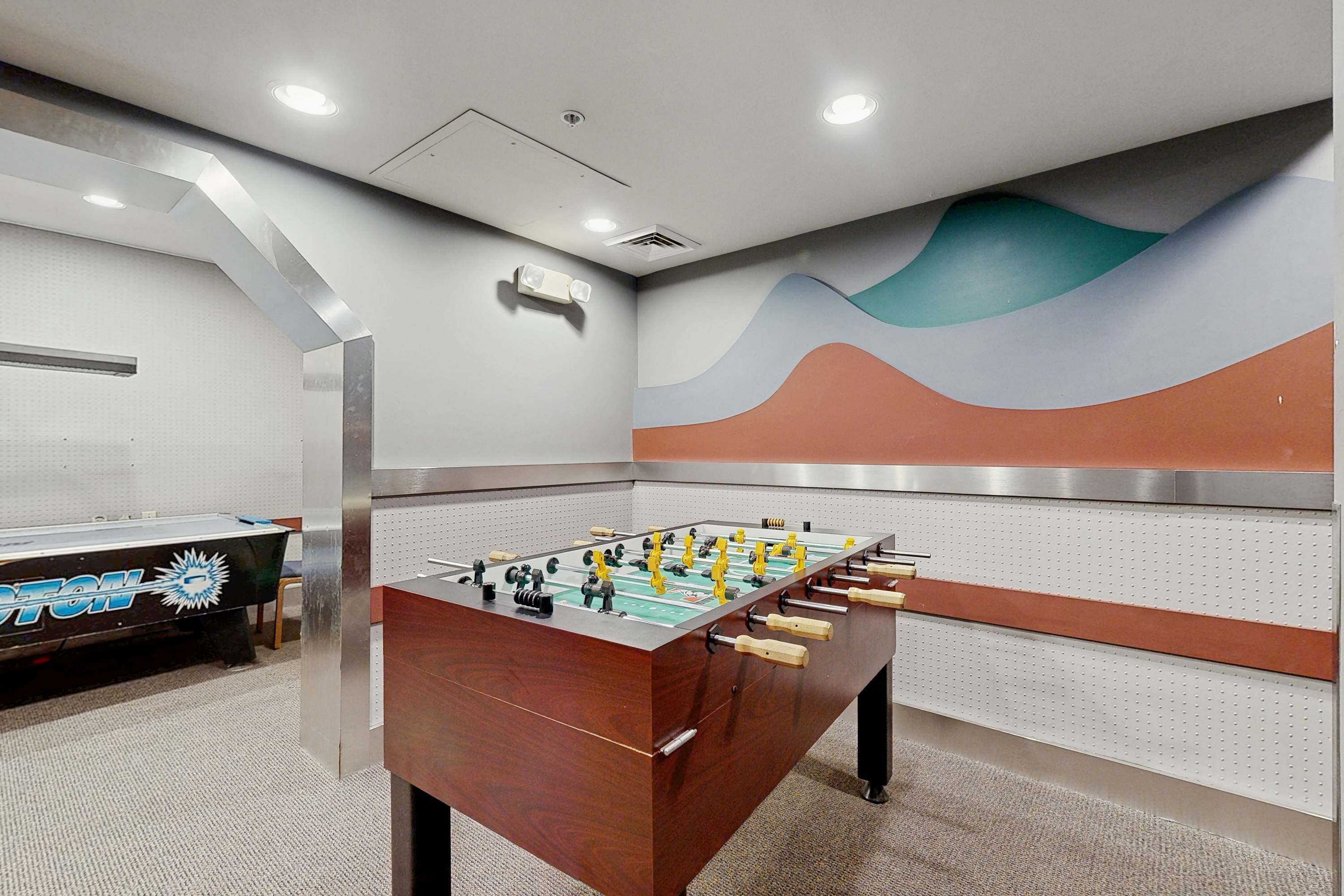 A foosball table in a room with a wall-mounted pegboard and a foosball table with a 'FOOTBALL' logo.