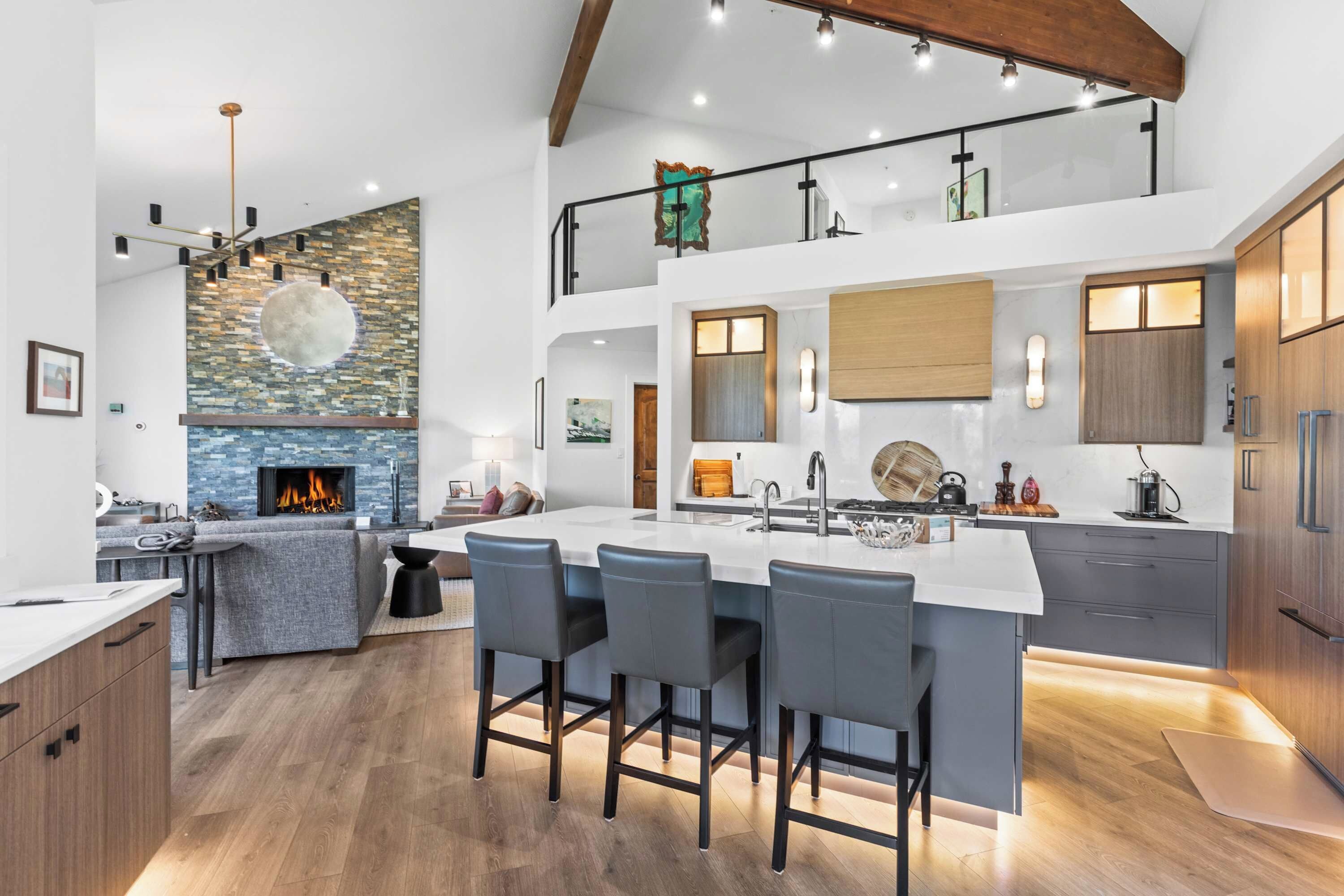 A modern kitchen with a central island, bar stools, a fireplace, and a loft area with a view.