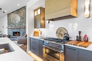 Eine moderne Küche mit Kamin aus Stein, Edelstahlgeräten und einer Holzausziehtafel.
