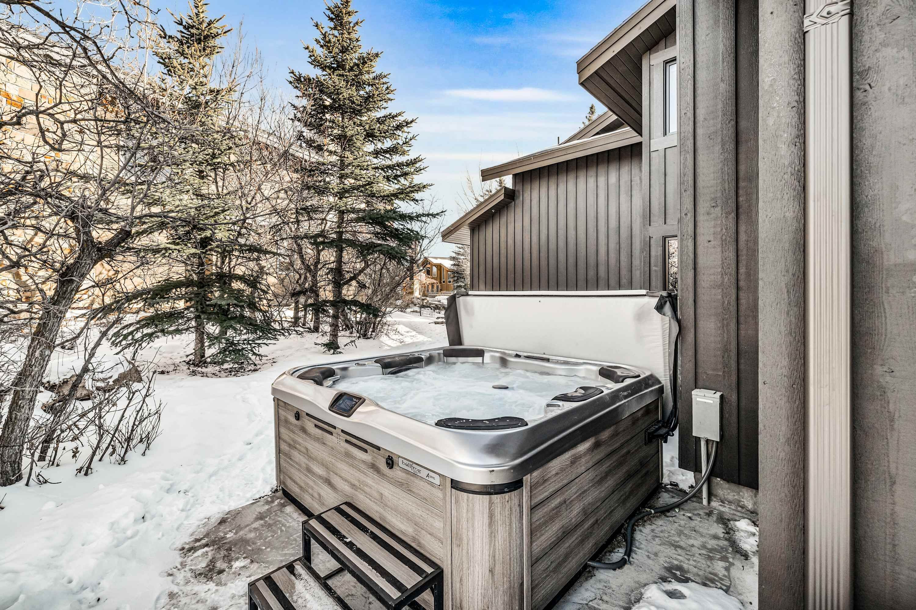A hot tub outside a building with a wooden exterior, snow on the ground, and bare trees.