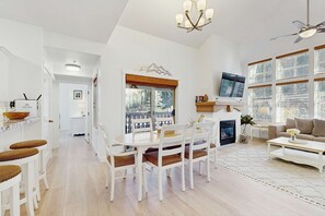 A spacious living area with a fireplace, a dining table with chairs, a sofa, and a TV mounted on the wall. - Relaxing mountain-view condo with shared hot tub, pool & more-walk to ski lifts (Solitude)