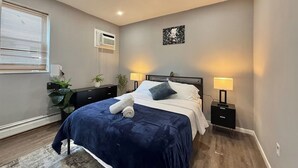 A bedroom with a bed, bedside lamps, a wall-mounted air conditioner, a window with blinds, and a small plant. - Modern apartment close to NYC (North Bergen)