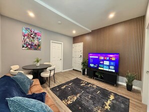 Un salon comprenant un téléviseur, un canapé, des fauteuils, une table basse et un mur décoratif.