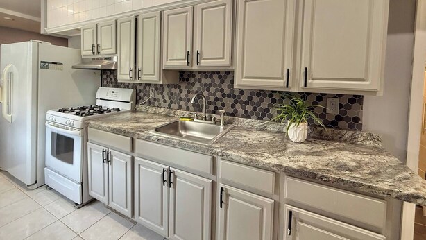 A kitchen with white cabinets, a granite countertop, a stainless steel sink, a stove, and a tiled backsplash. - Modern apartment close to NYC (North Bergen)