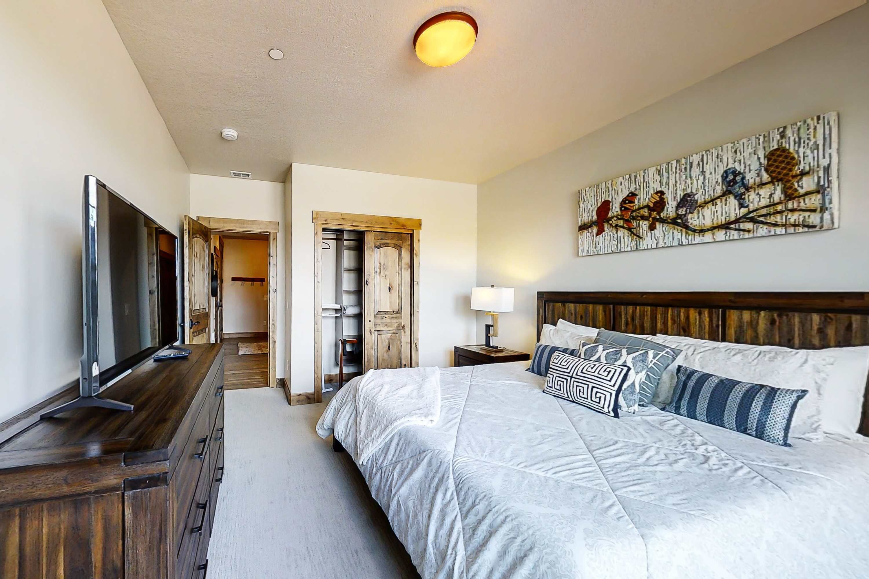 Een slaapkamer met een groot bed, een televisie, een houten dressoir, een schilderij en een gang naar een andere kamer.