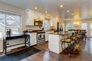 A modern kitchen with white cabinets, stainless steel appliances, a central island with bar stools, and a dining area with a chandelier. - Modern Townhouse with Jetted Tub & Private Deck - Close to Four Ski Areas (Cottonwood Heights)