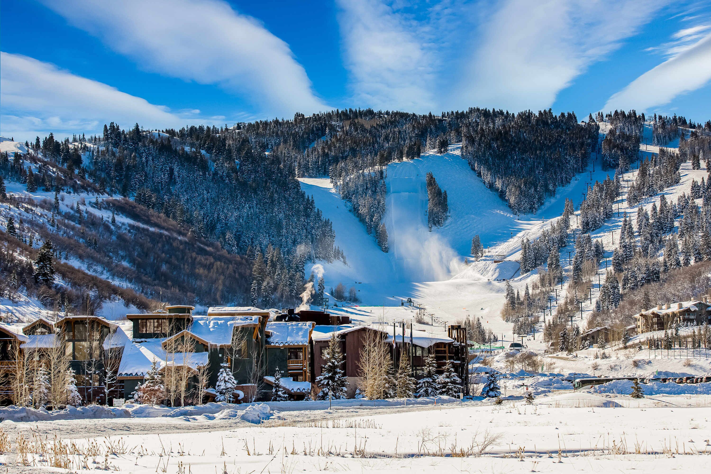 Une station de montagne enneigée, avec des chalets, des pistes de ski et un ciel d’un bleu limpide.