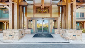 Entrada de una cabaña con base de piedra, vigas de madera y puerta de cristal.