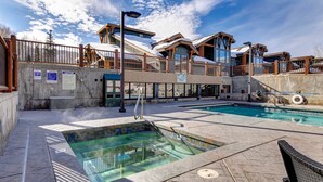 Un área de piscina con jacuzzi, terraza techada y un edificio con amplios ventanales.