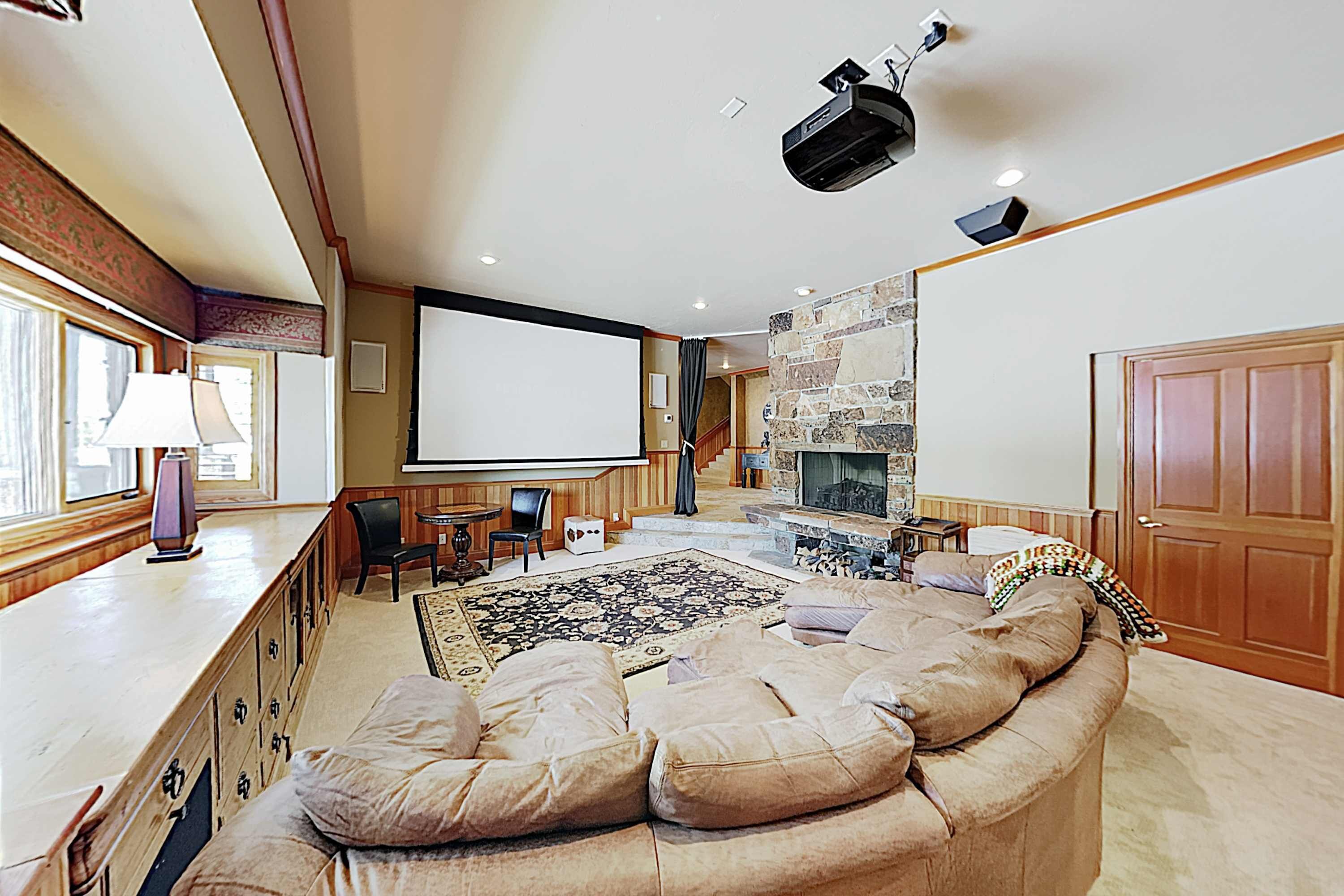 A spacious living room with a large sectional sofa, a fireplace, a stone accent wall, a projector, and a large window.