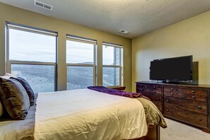 A bedroom with a bed, a dresser, a television, and large windows. - Home with  fireplace, private hot tub, shared pool, game and fitness facilities (Kamas)