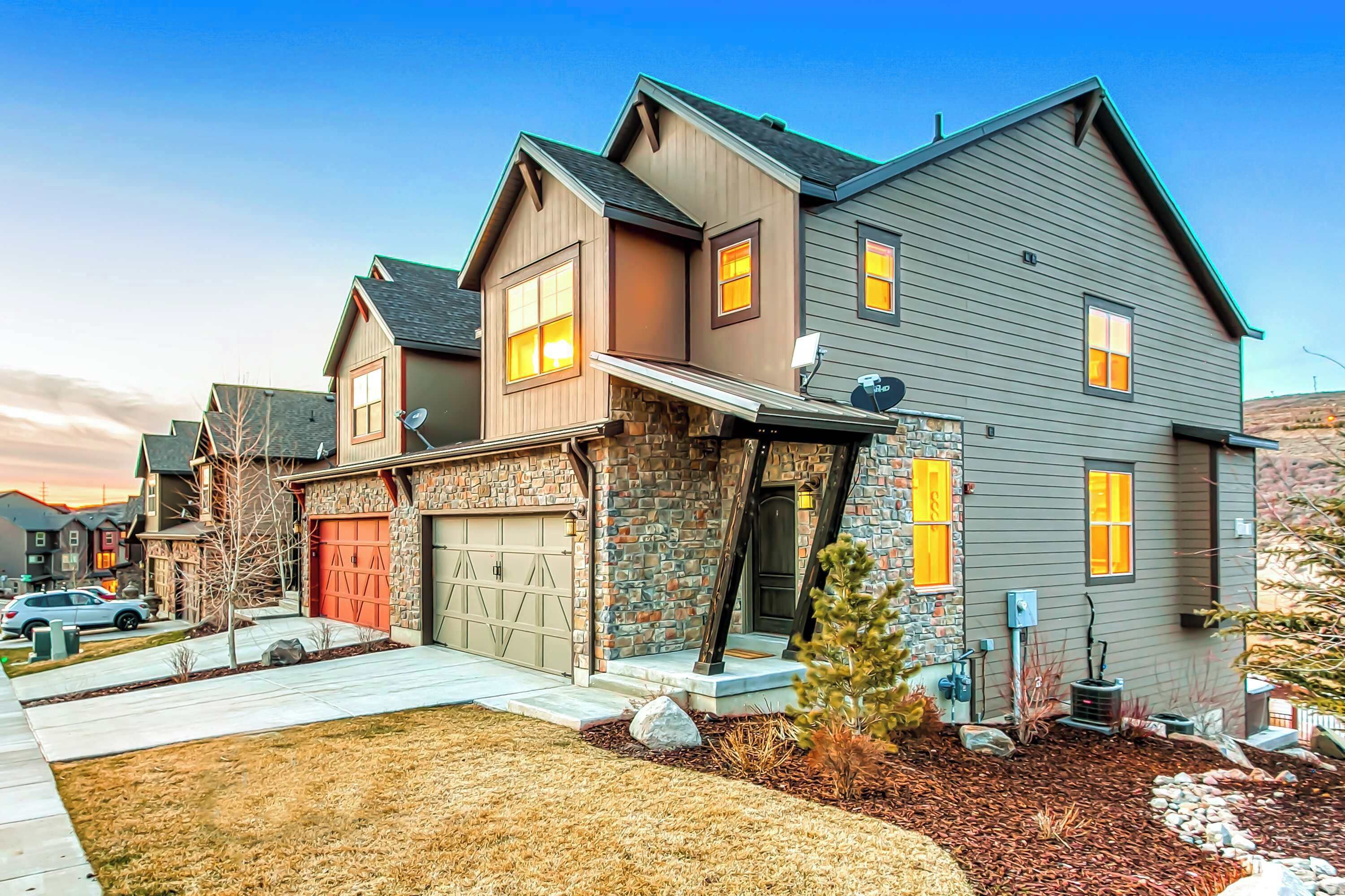 A two-story house with a stone facade, a red garage door, and a well-maintained lawn.