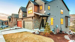 A two-story house with a stone facade, a red garage door, and a well-maintained lawn. - Home with  fireplace, private hot tub, shared pool, game and fitness facilities (Kamas)