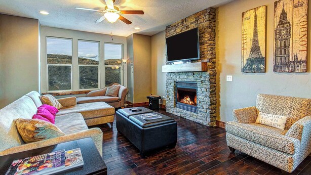 A living room with a stone fireplace, a flat-screen TV, and a sofa set. - Home with  fireplace, private hot tub, shared pool, game and fitness facilities (Kamas)