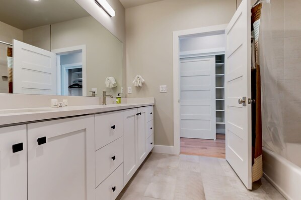 Een moderne badkamer met een grote spiegel, witte kasten en een inloopkast.
