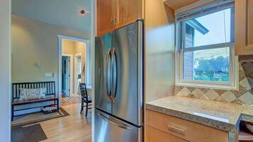A kitchen with a stainless steel refrigerator, wooden cabinets, a granite countertop, and a window with a view.