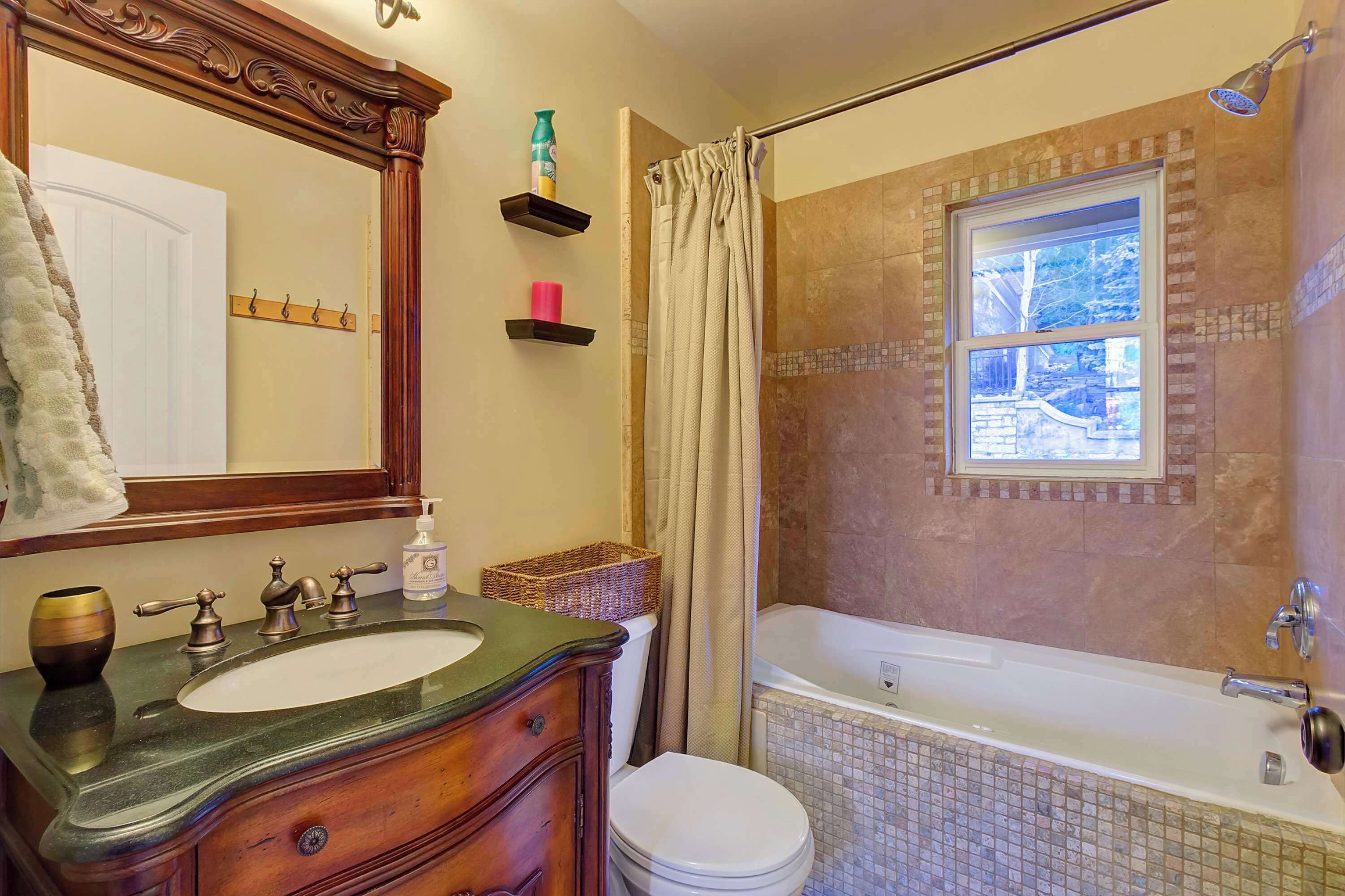 Ein Badezimmer mit Waschtisch, Becken, Spiegel, Toilette, Badewanne, Duschvorhang und einem Fenster.