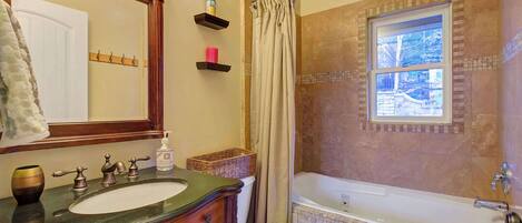 Ein Badezimmer mit Waschtisch, Becken, Spiegel, Toilette, Badewanne, Duschvorhang und einem Fenster.