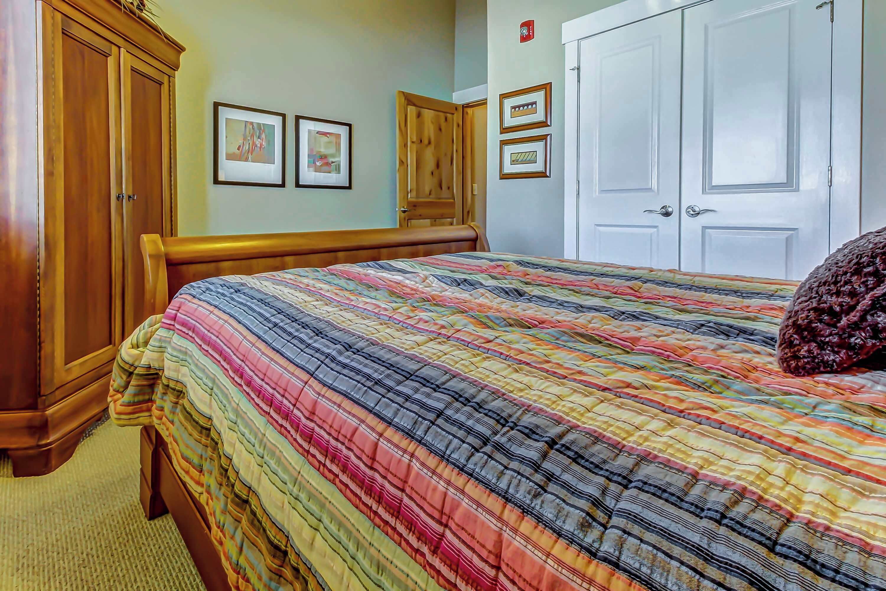 A bedroom with a bed, wooden wardrobe, and two framed pictures on the wall.