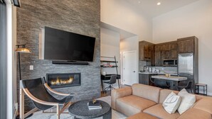 A modern living room with a fireplace, a flat-screen TV, a sofa, and a dining area with a kitchen in the background. - Townhouse in Hideout with foosball table (Hideout)