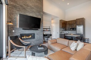 A modern living room with a fireplace, a flat-screen TV, a sofa, and a dining area with a kitchen in the background. - Townhouse in Hideout with foosball table (Hideout)