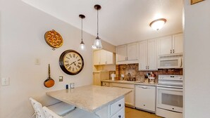 Una cocina con gabinetes blancos, un reloj, luces colgantes y un microondas.