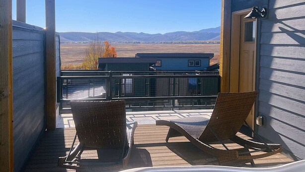 Eine Veranda mit zwei Korbstühlen, Blick auf ein blaues Haus und einem Metallgeländer.