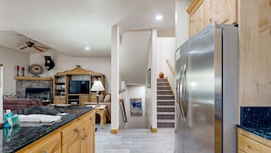 Una cocina con armarios de madera, un refrigerador de acero inoxidable, una chimenea de piedra y una escalera que conduce a otro nivel.