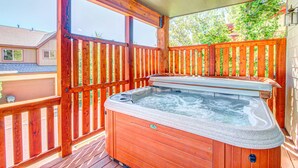 En træterrasse med jacuzzi, trægelændere og et hus i baggrunden.