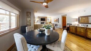 Un coin repas avec une table ronde, des chaises, un ventilateur de plafond et une cuisine en arrière-plan.