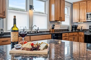 A kitchen with wooden cabinets, a granite countertop, a wine bottle, and a charcuterie board. - Harmony House/Walk to Downtown/Parking/Balcony (Portland)