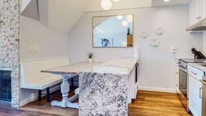 Una cocina moderna con encimera de mármol, armarios blancos, horno empotrado y una lámpara colgante.