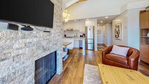 Una sala de estar moderna con chimenea de piedra, televisor de pantalla plana, sofá de cuero y mesa de centro de madera.