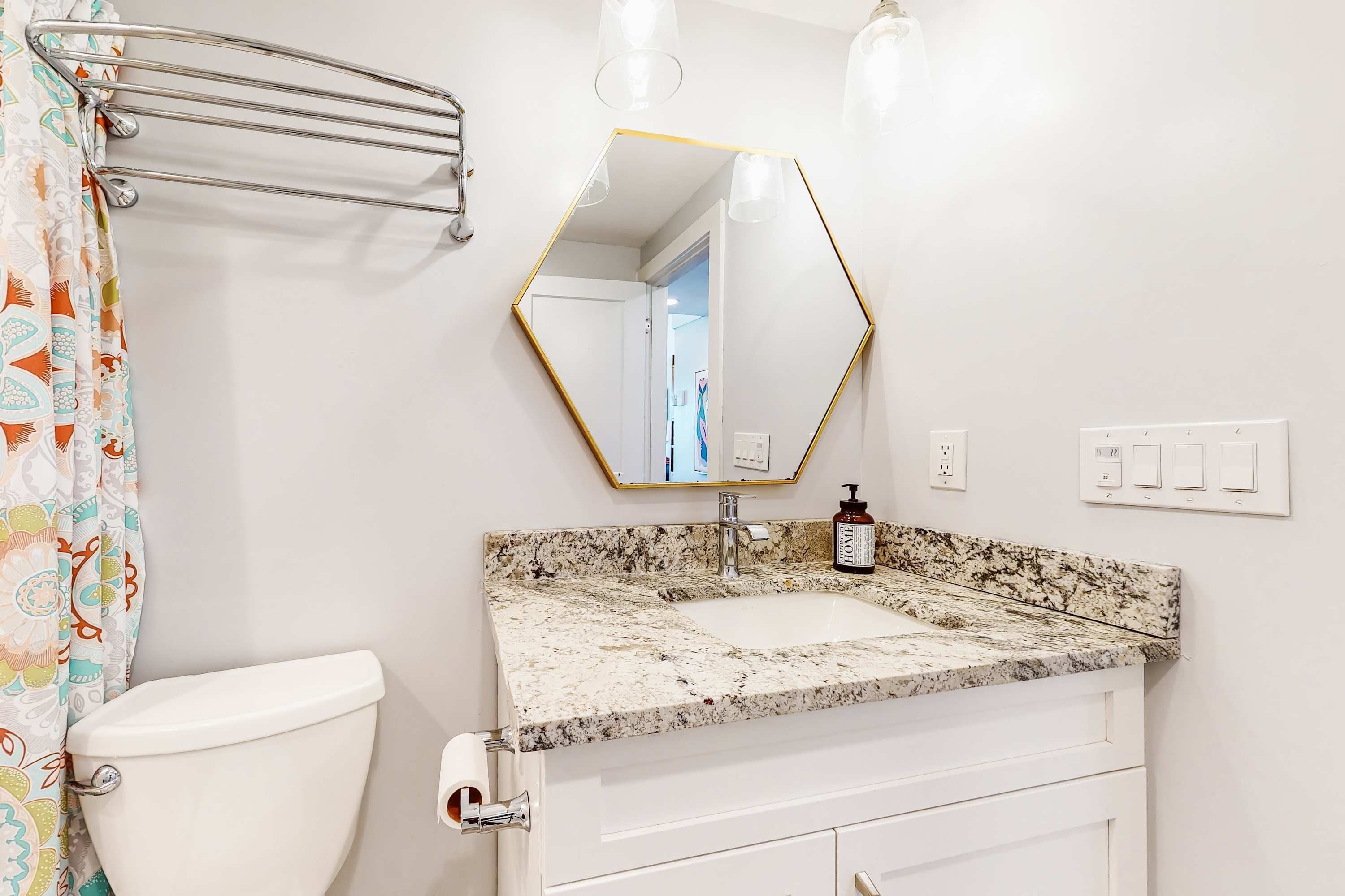 A bathroom with a toilet, a sink with a marble countertop, a mirror with a gold frame, and a shower curtain with a floral pattern.