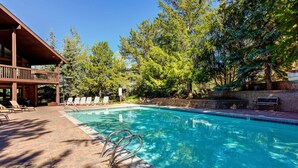 Une piscine à l’eau claire, entourée d’arbres et bordée d’un bâtiment doté d’un balcon.