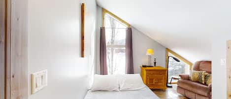 A bedroom with a bed, a wooden dresser, a chair, and a window with curtains.