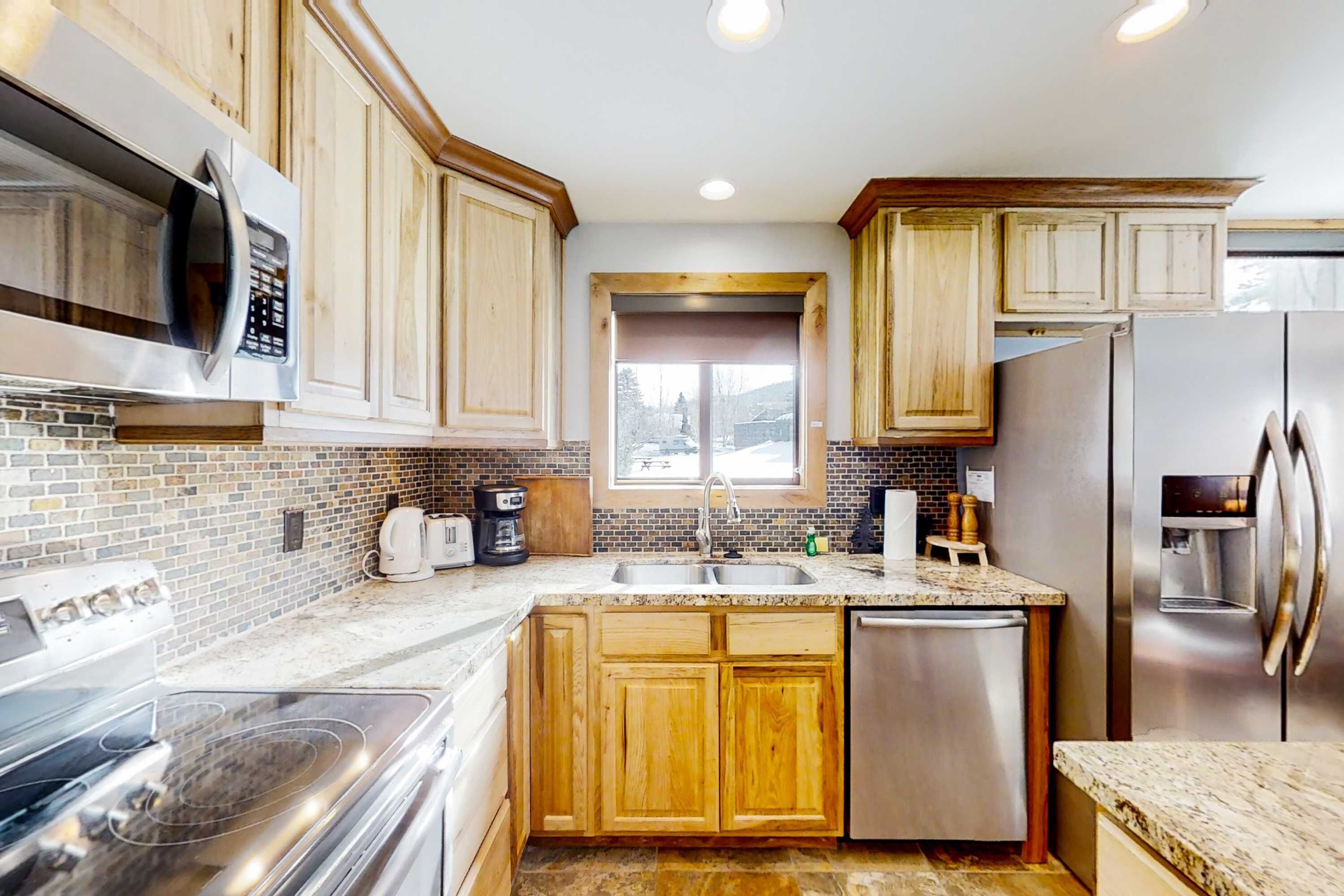 A kitchen with wooden cabinets, stainless steel appliances, a window, and a brick backsplash.
