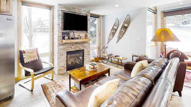 A modern living room with a fireplace, leather sofa, and a television mounted on the wall. - Remodeled mountainside home with outdoor heated pool & hot tub - walk everywhere (Park City)
