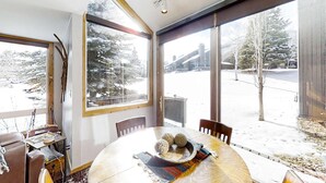 A dining area with a round table, chairs, and a view of a snowy landscape through large windows. - Remodeled mountainside home with outdoor heated pool & hot tub - walk everywhere (Park City)